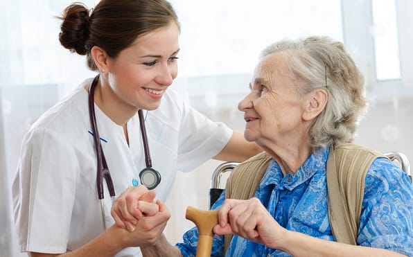 A nurse providing support by holding the hand of an elderly woman with a cane, who is seated in a wheelchair, fostering a compassionate and caring connection between caregiver and patient.
