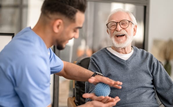 An occupational therapist guiding a joyful senior in utilizing a therapy ball during an engaging occupational therapy session, promoting physical activity, coordination, and therapeutic benefits for enhanced well-being.