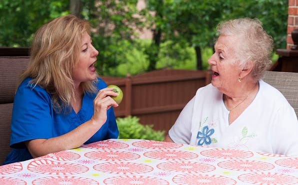 A speech therapist incorporating an apple into a speech therapy session with an elderly stroke patient, utilizing it as a tool for speech exercises and oral motor skill development, fostering communication and rehabilitation.